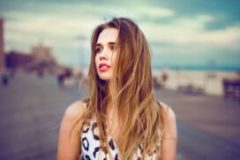 Beautiful young girl walking on city ocean beach boardwalk at sunset time and wind blowing up her hair. Woman looking to the side outdoors.